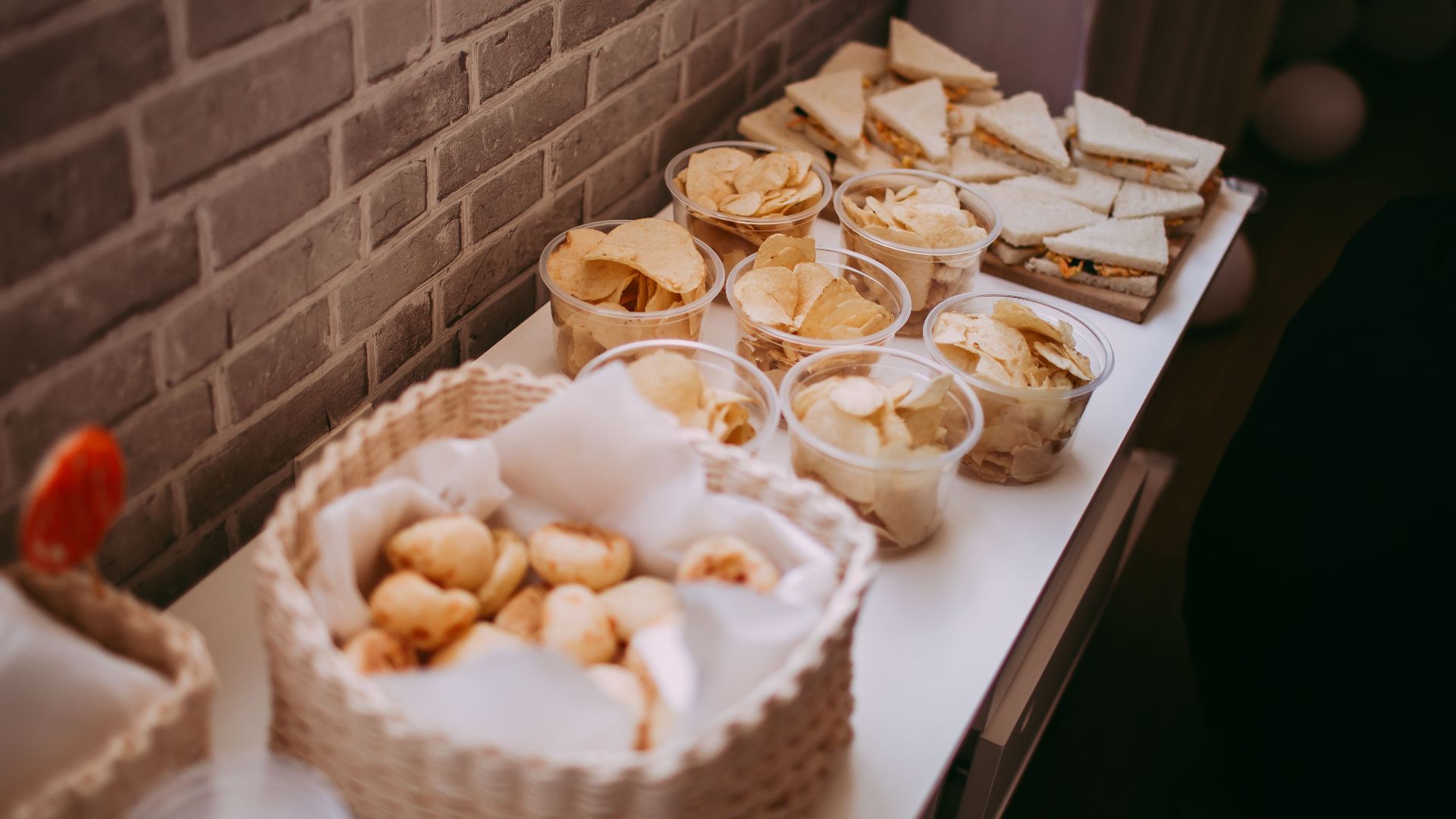 A variety of snacks and sandwiches on a buffet table against a brick wall.