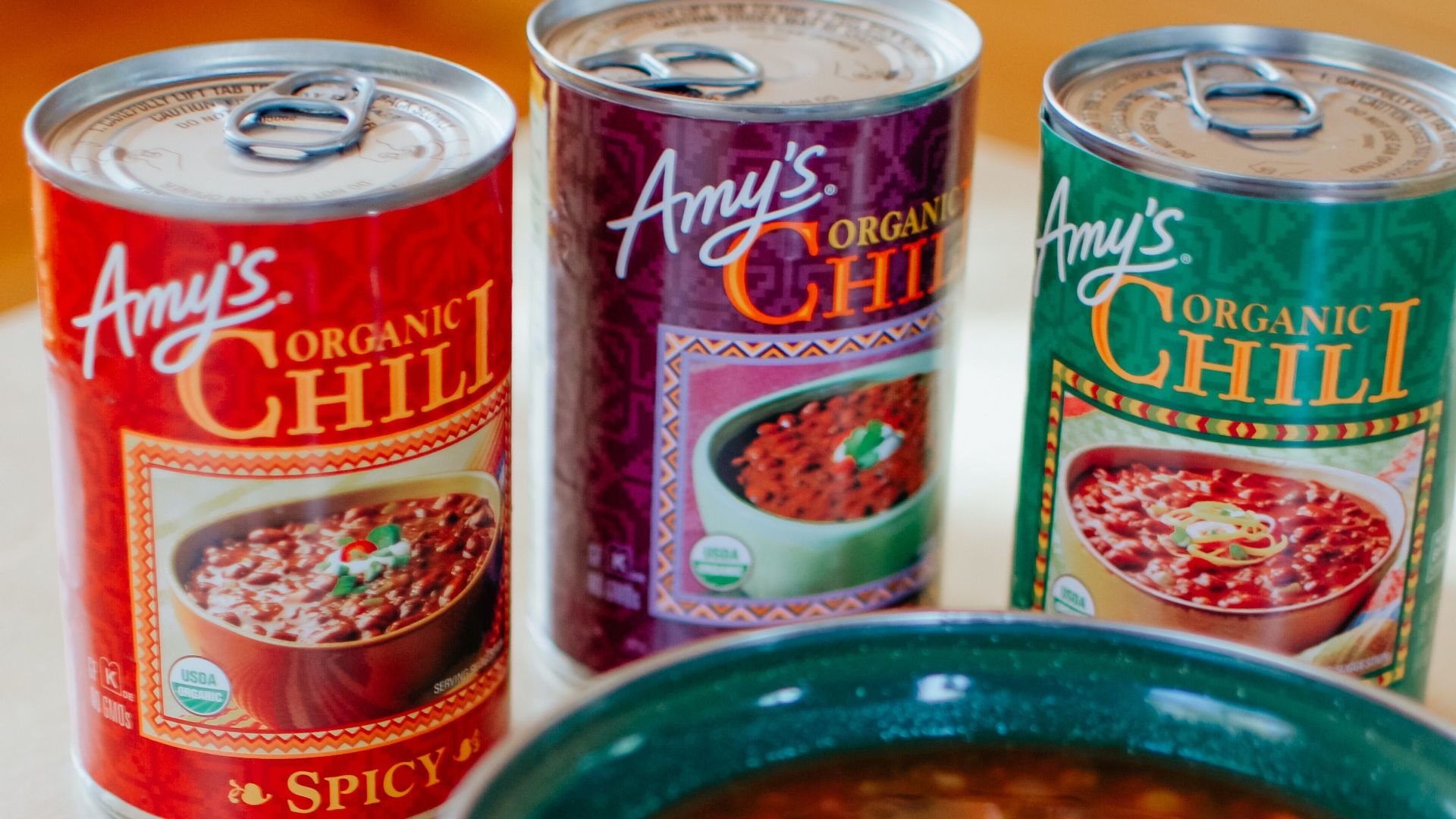 A vertical shot of organic chili served in a ceramic bowl, with canned chili options nearby.