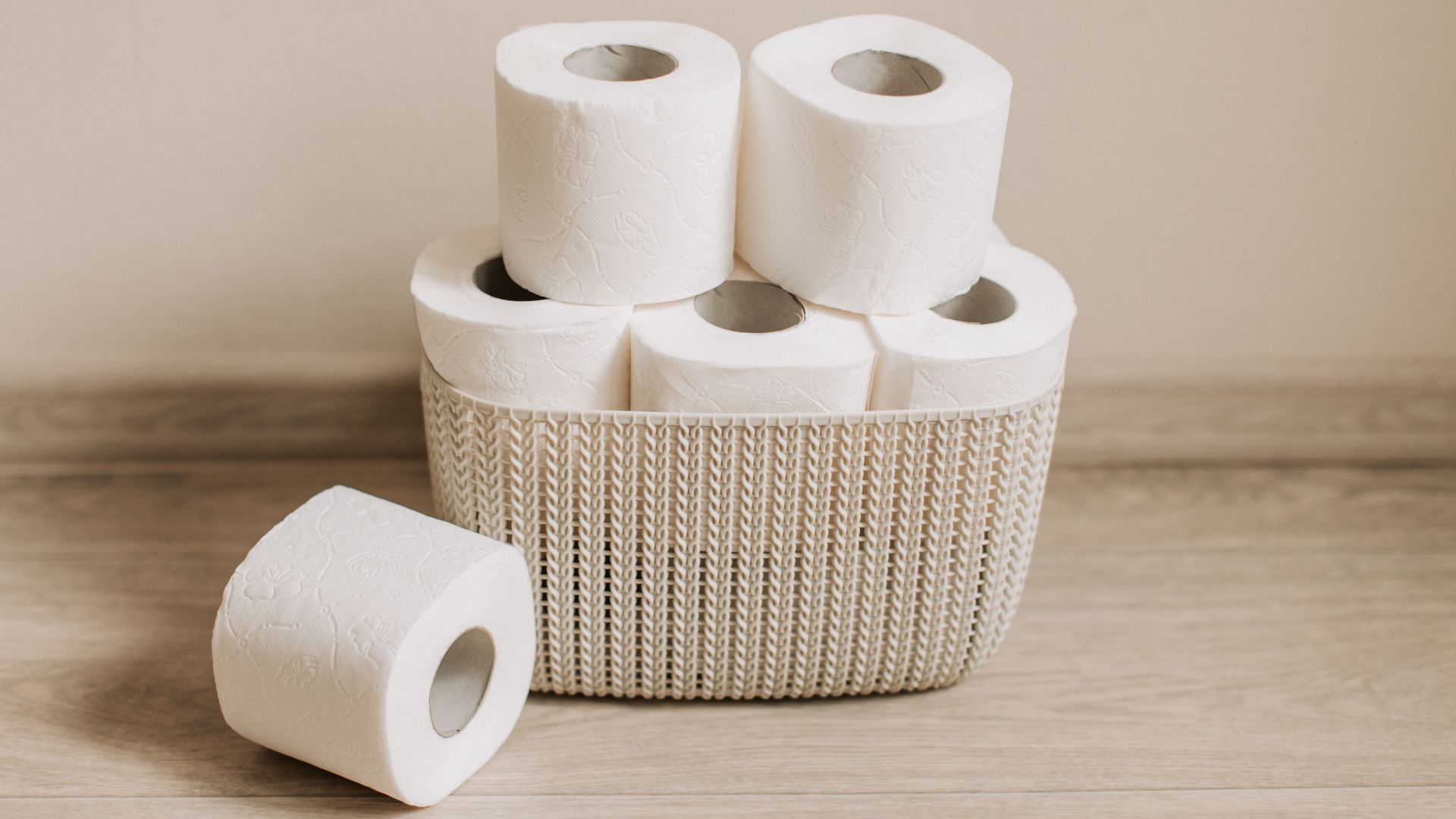 Basket of white toilet paper rolls neatly arranged on a wooden floor.