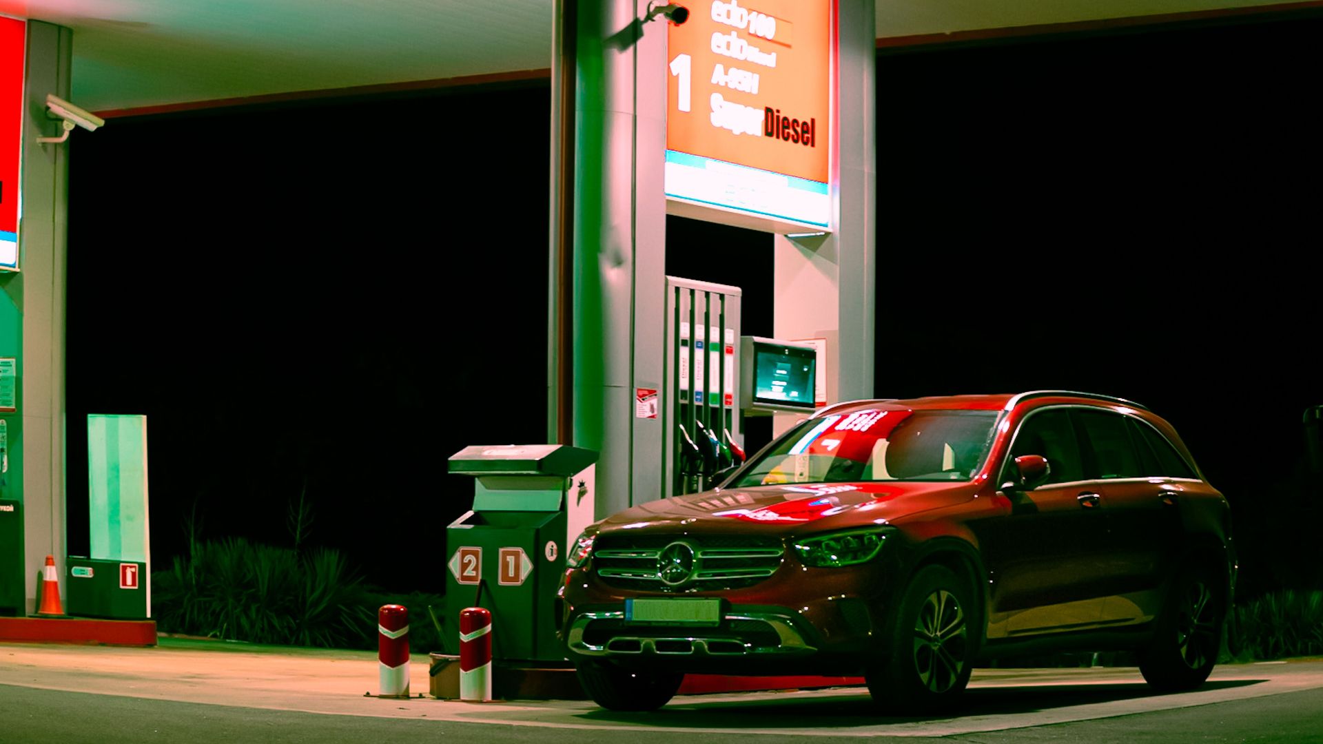 A sleek car parked at a brightly lit gas station under a neon sign during nighttime.