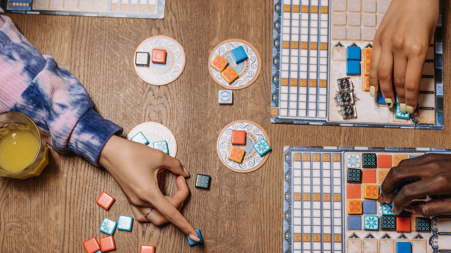 People enjoying a strategic board game on a wooden table with drinks, showcasing social interaction.