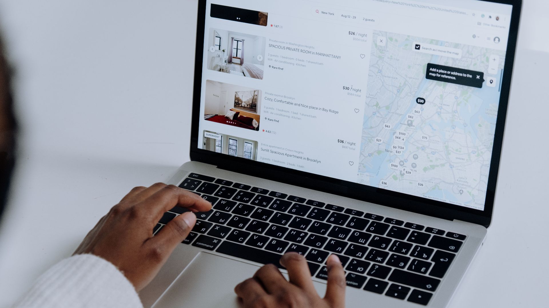 Hands typing on laptop searching Airbnb for accommodation options with map view.