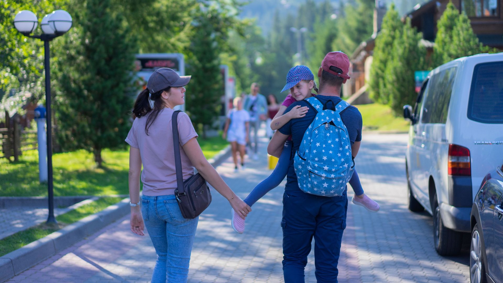 Parents walking with their daughter in a picturesque mountain village, enjoying a sunny day outdoors.
