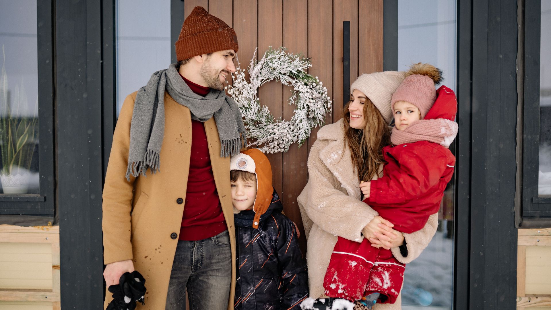 Family enjoying winter holiday outside, posing by a festive door with a Christmas wreath.