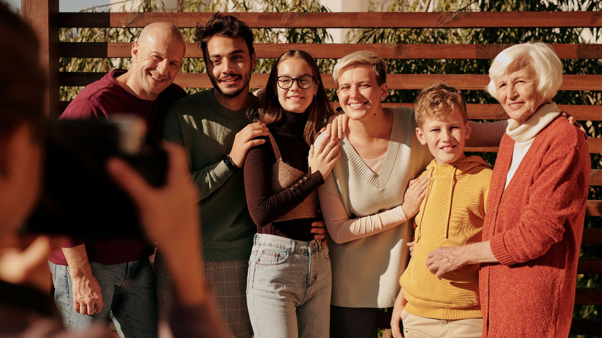 A joyful family portrait featuring multiple generations smiling outdoors in daylight.