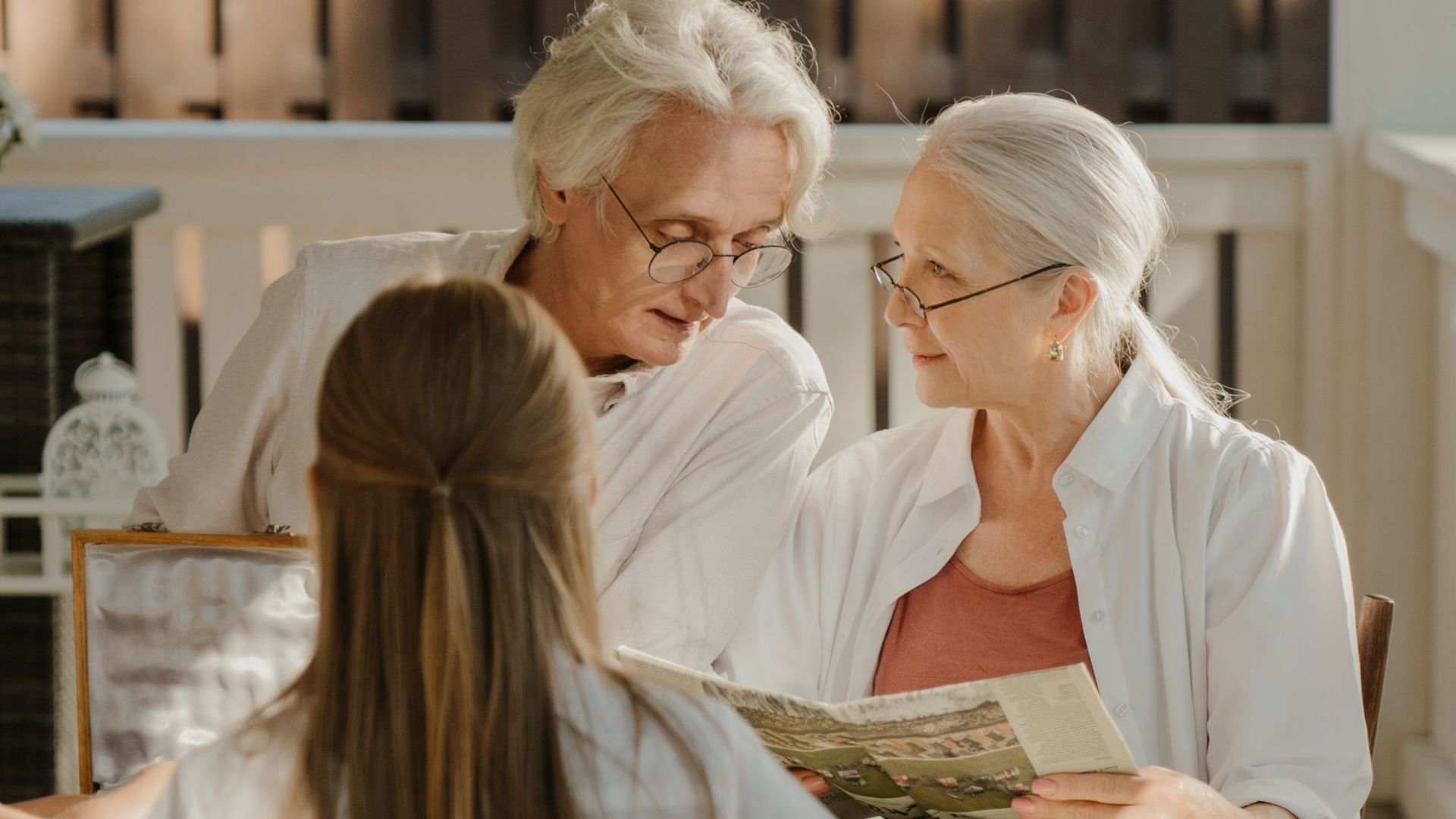 Elderly couple sitting together outside, sharing a tender moment on a veranda with family.