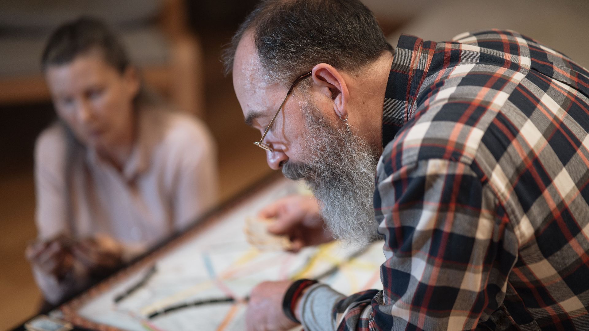 A bearded man and a woman engaging in an intense board game at home. Captured indoors.