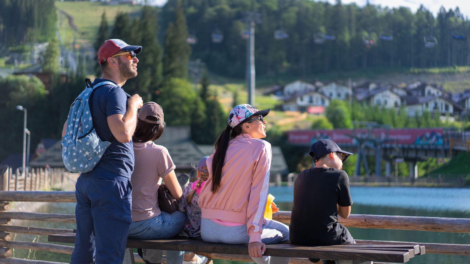 A family enjoys a sunny day sitting on a bench in Bukovel, Ukraine, with scenic mountain views.