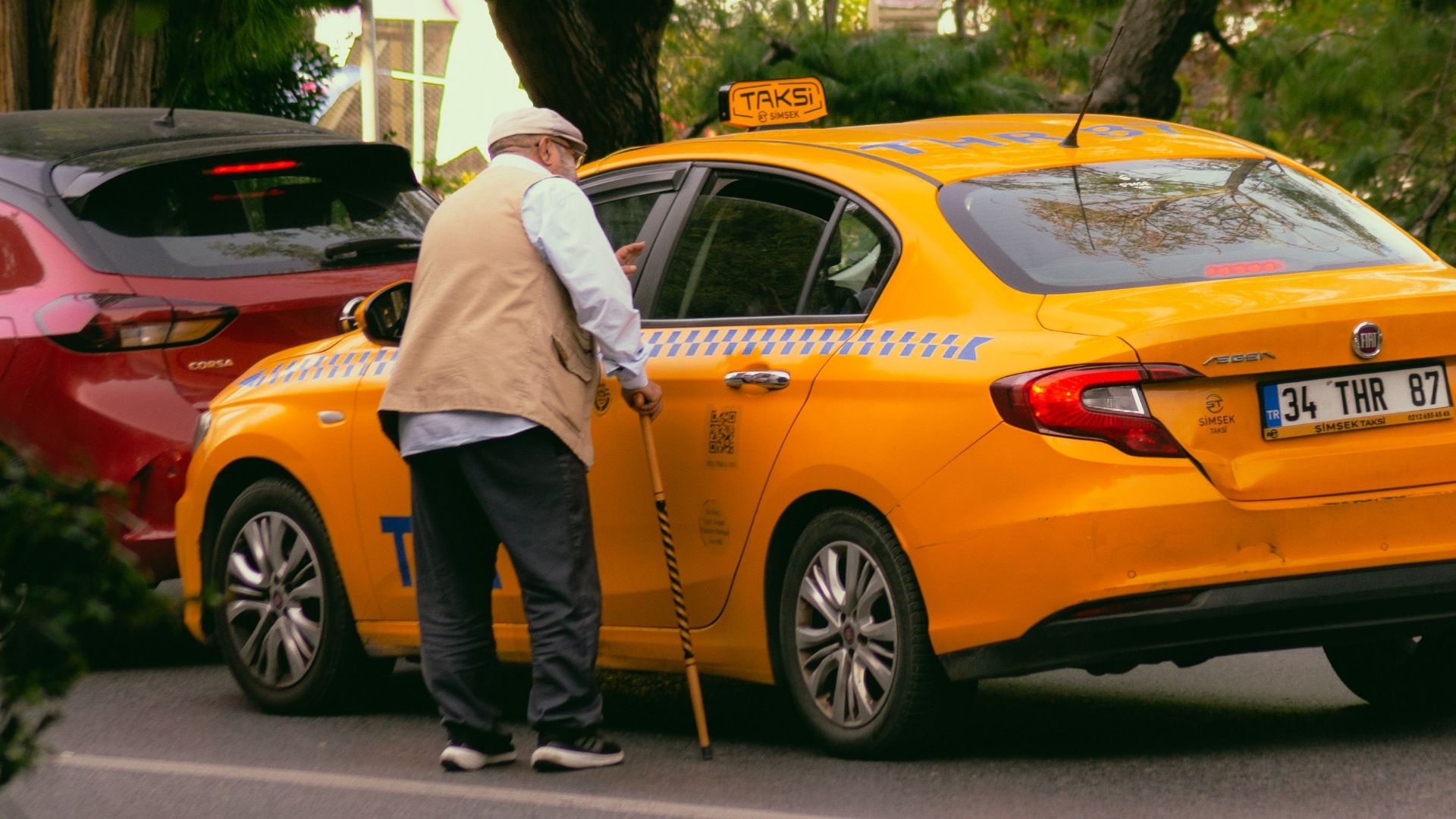 Elderly man with cane getting into a yellow taxi on a city street.