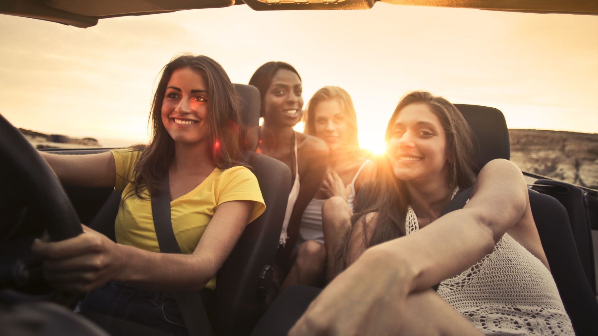 Four friends share smiles and laughter in a convertible during a sunset road trip in Malta.
