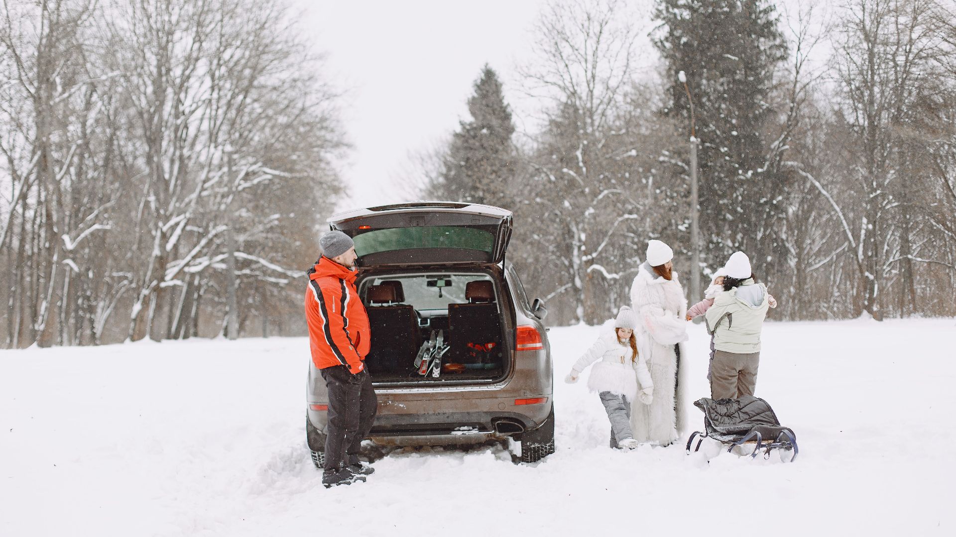 Family in winter gear preparing for outdoor adventure with SUV in snow-covered landscape.