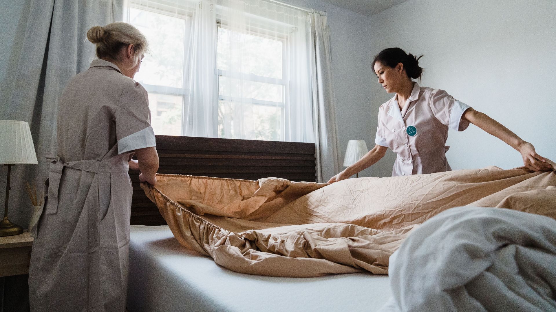Two housekeepers professionally making a bed in a bright, comfortable room.