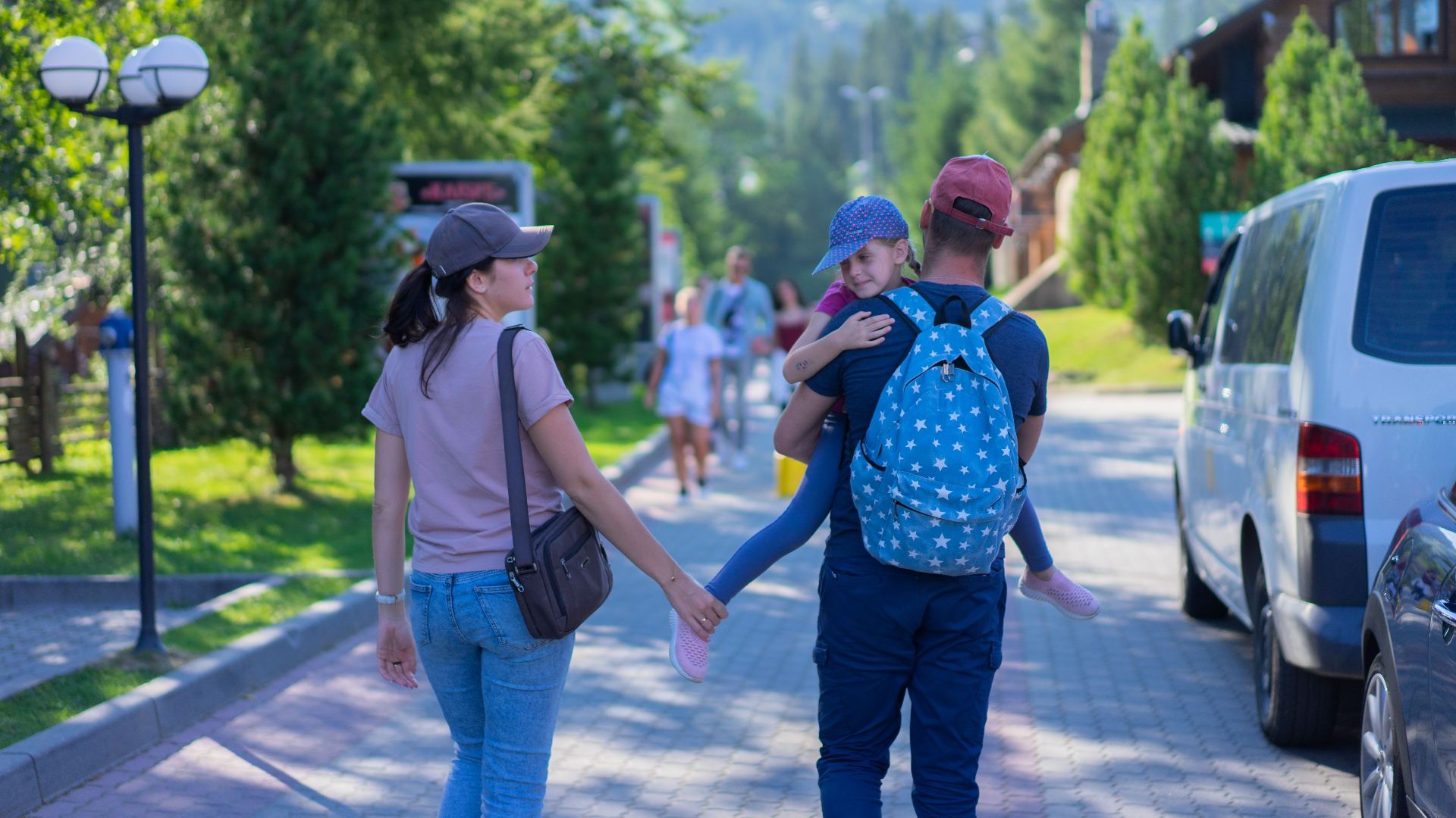 Parents walking with their daughter in a picturesque mountain village, enjoying a sunny day outdoors.