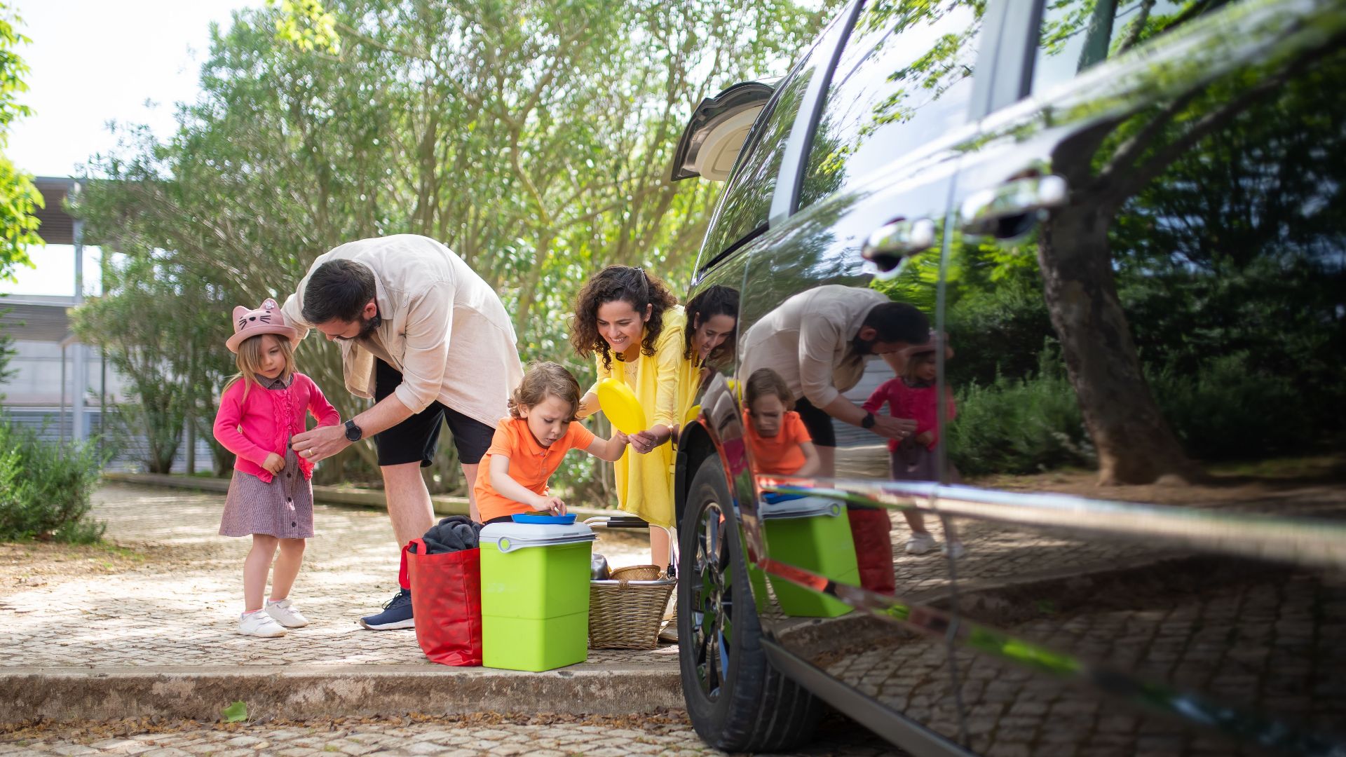 A family prepares for a joyful picnic outing in a sunny park with a black car, reflecting happiness and bonding.