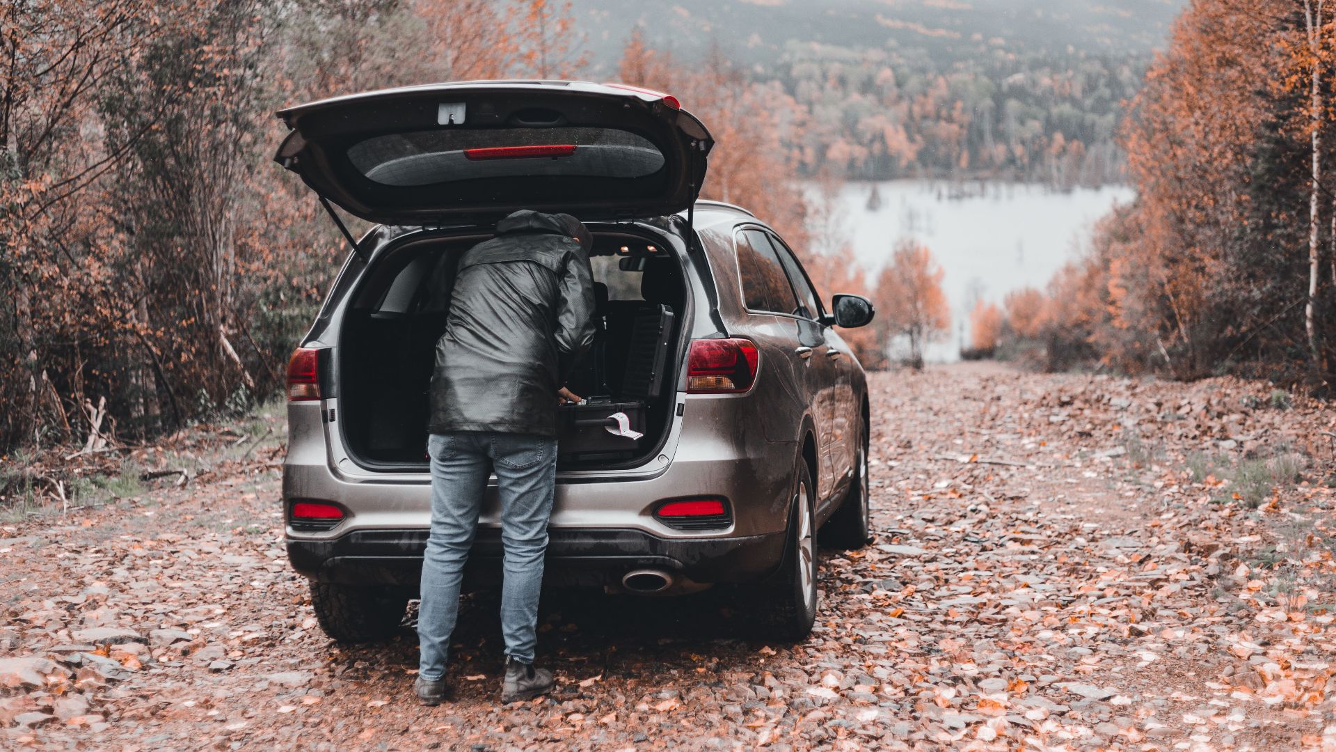 A person in a bubble jacket unloads an SUV in stunning fall scenery.