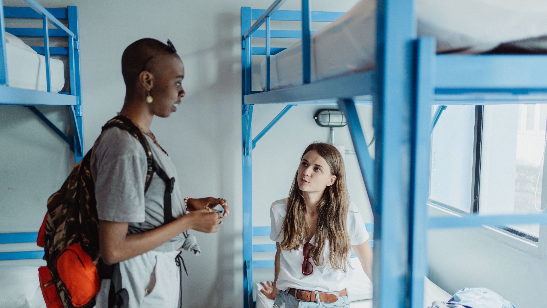 Two travelers converse in a hostel dormitory, showcasing diverse culture and adventure.