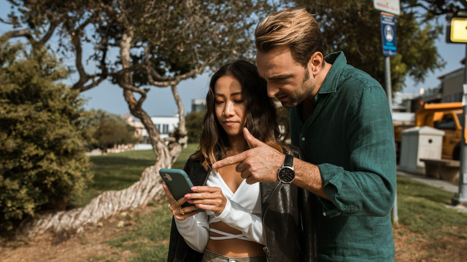 A man and woman using a smartphone together in a city park during daytime.