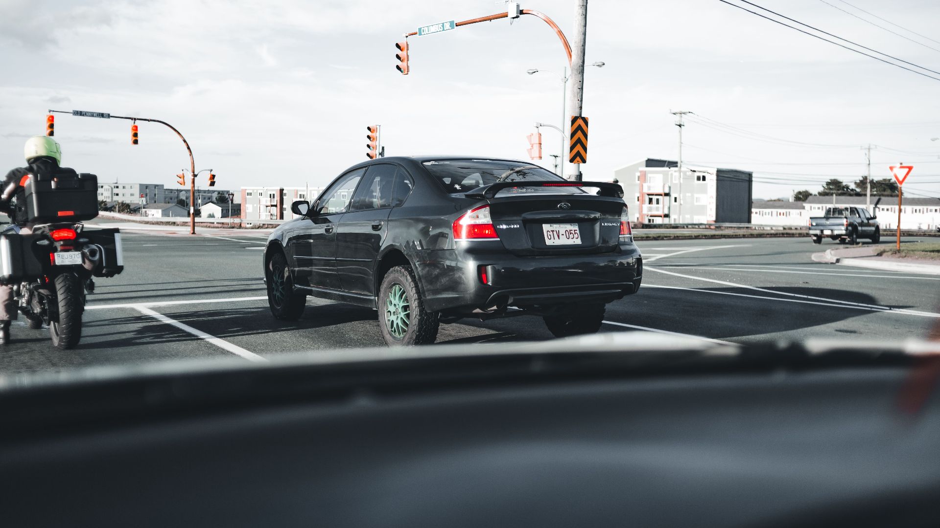 A motorcycle and car wait at a busy city intersection under traffic lights.