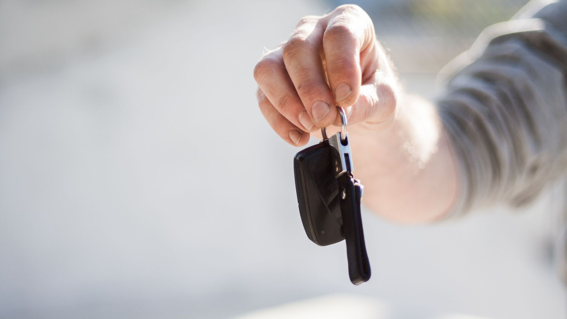 Close-up of a hand handing over car keys, signifying purchase or rental.