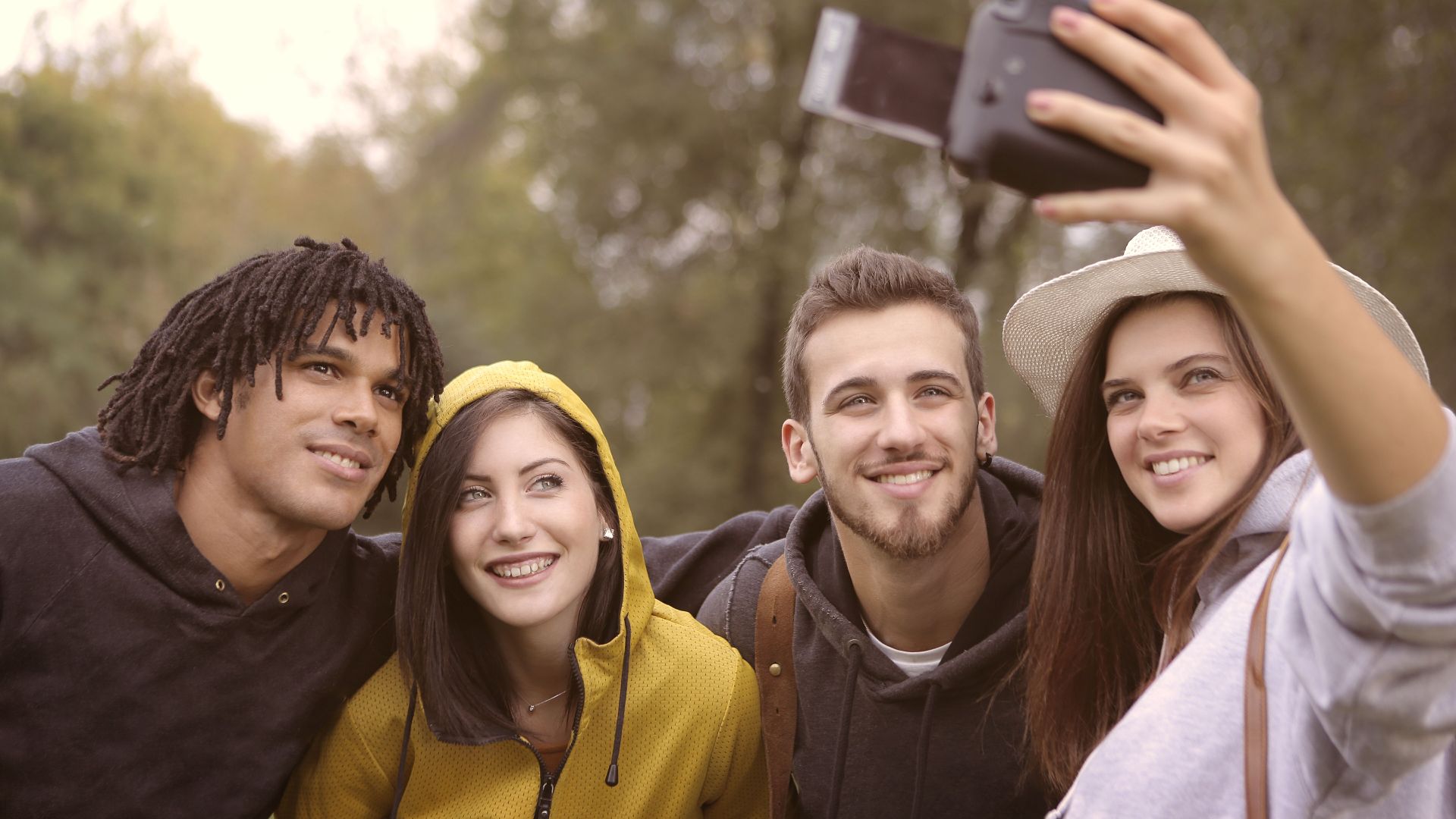 Cheerful group of young people smiling while taking selfie on camera in forest