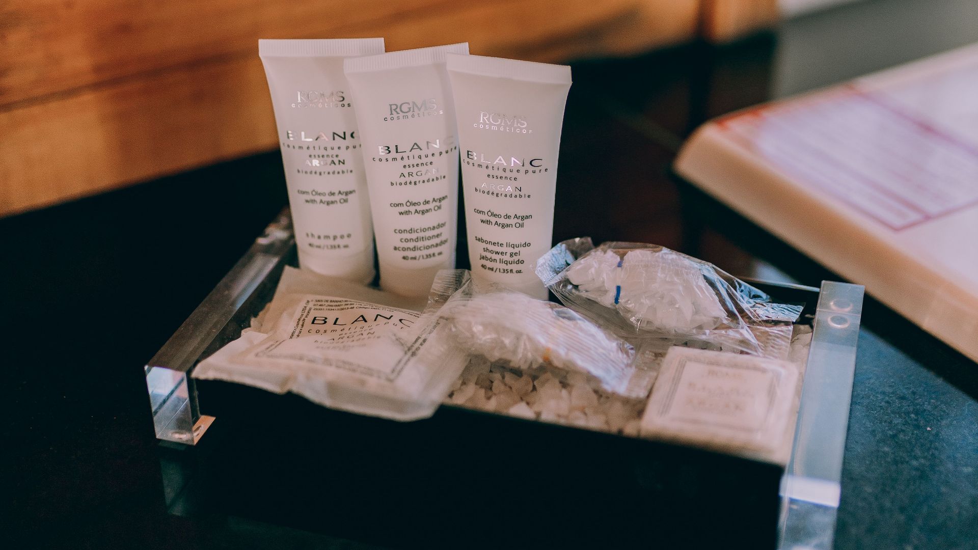 Elegant hotel bathroom amenities placed on a wooden counter beside a chrome faucet.