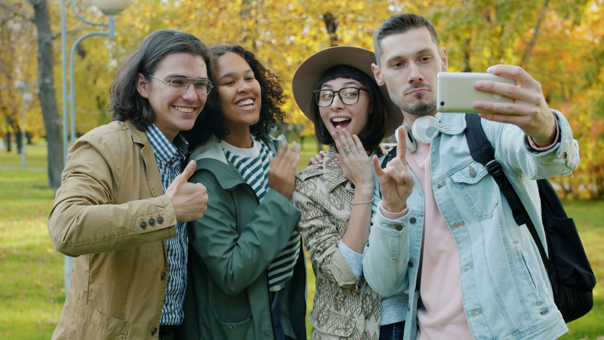 Four friends happily taking a selfie together in a beautiful autumn park setting.