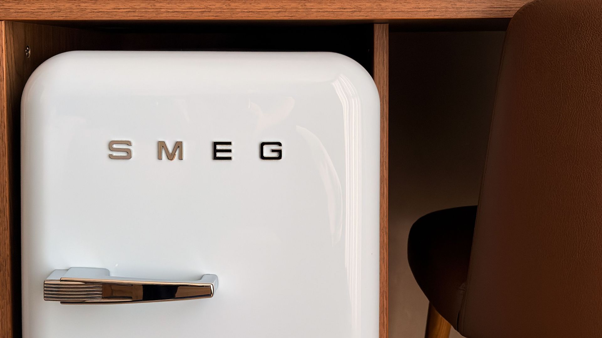 Stylish white SMEG fridge integrated under a wooden desk in a contemporary room setting.