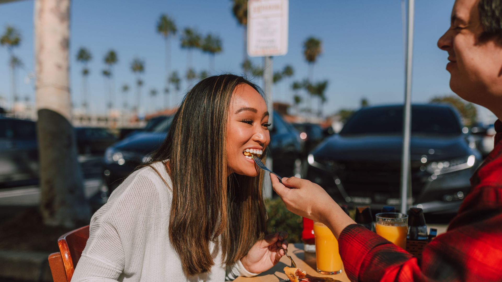 A couple enjoying a sunny brunch outdoors, sharing pancakes and juice, creating a sweet and joyful moment.