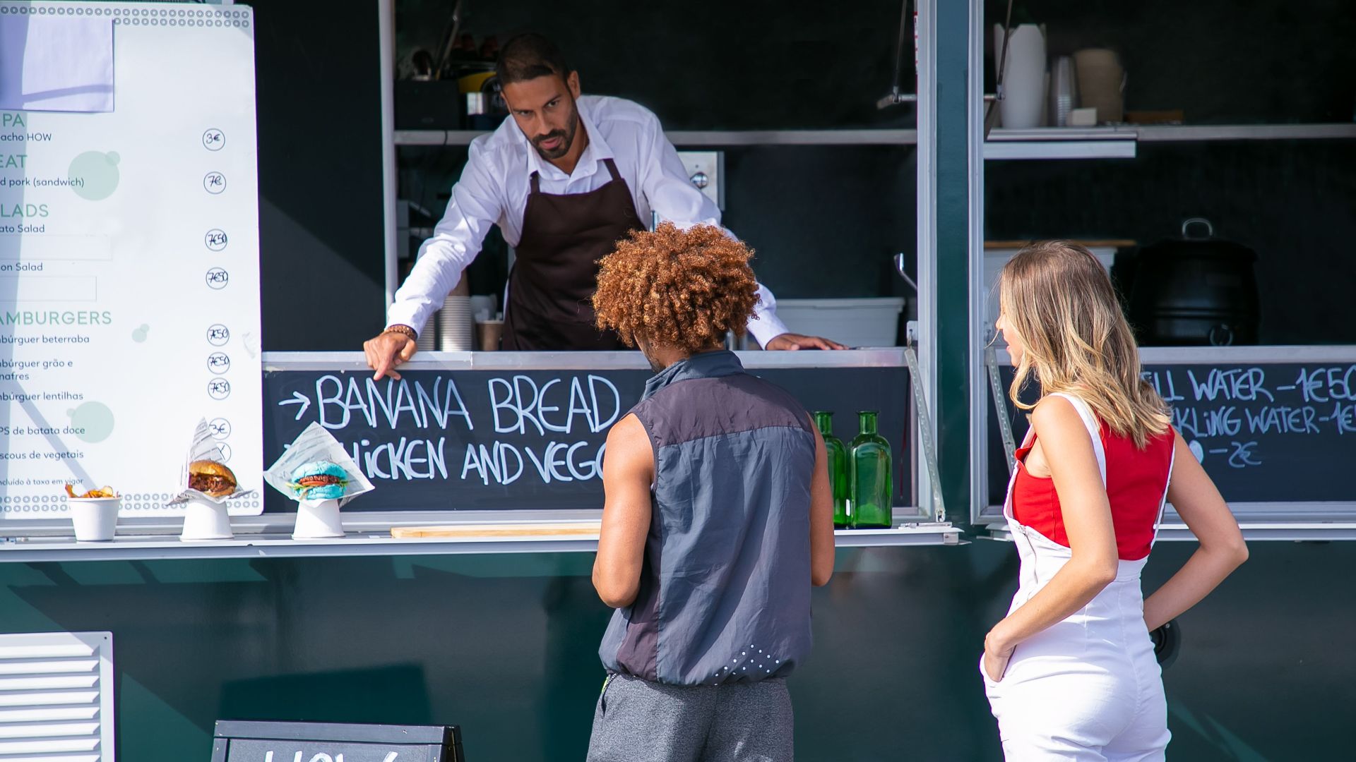 Ethnic salesman in uniform giving advice for choice of diverse customers of street food truck
