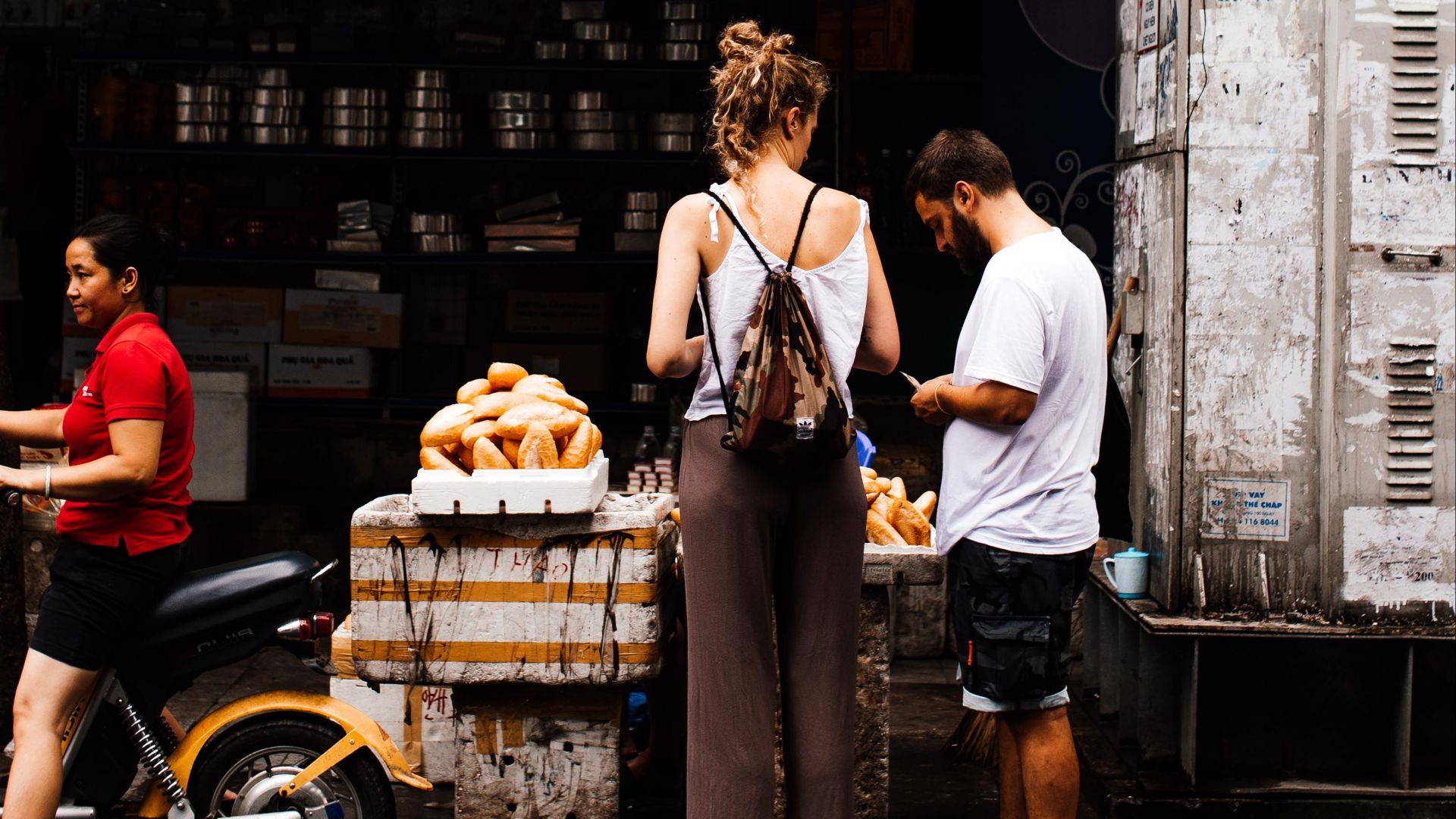 Two people buying baguettes at an outdoor street market stall.
