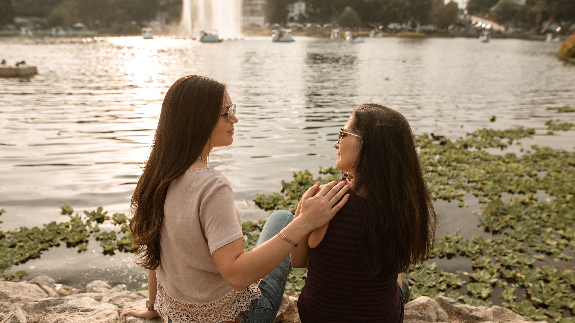 Two women sit by a lake, enjoying a moment of friendship and calm outdoors.