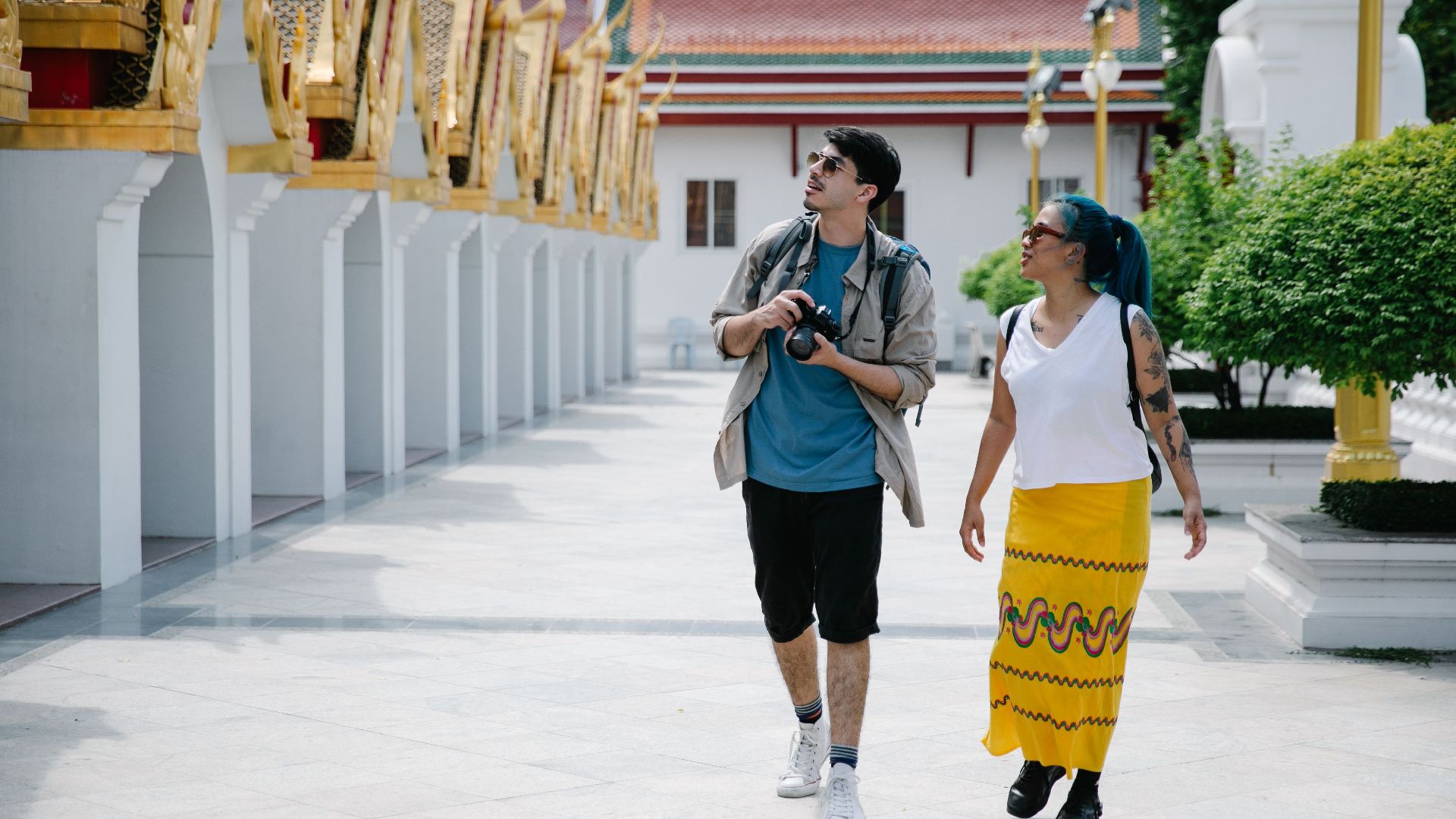 Two tourists walk and explore a traditional Thai temple, enjoying sightseeing and photography.