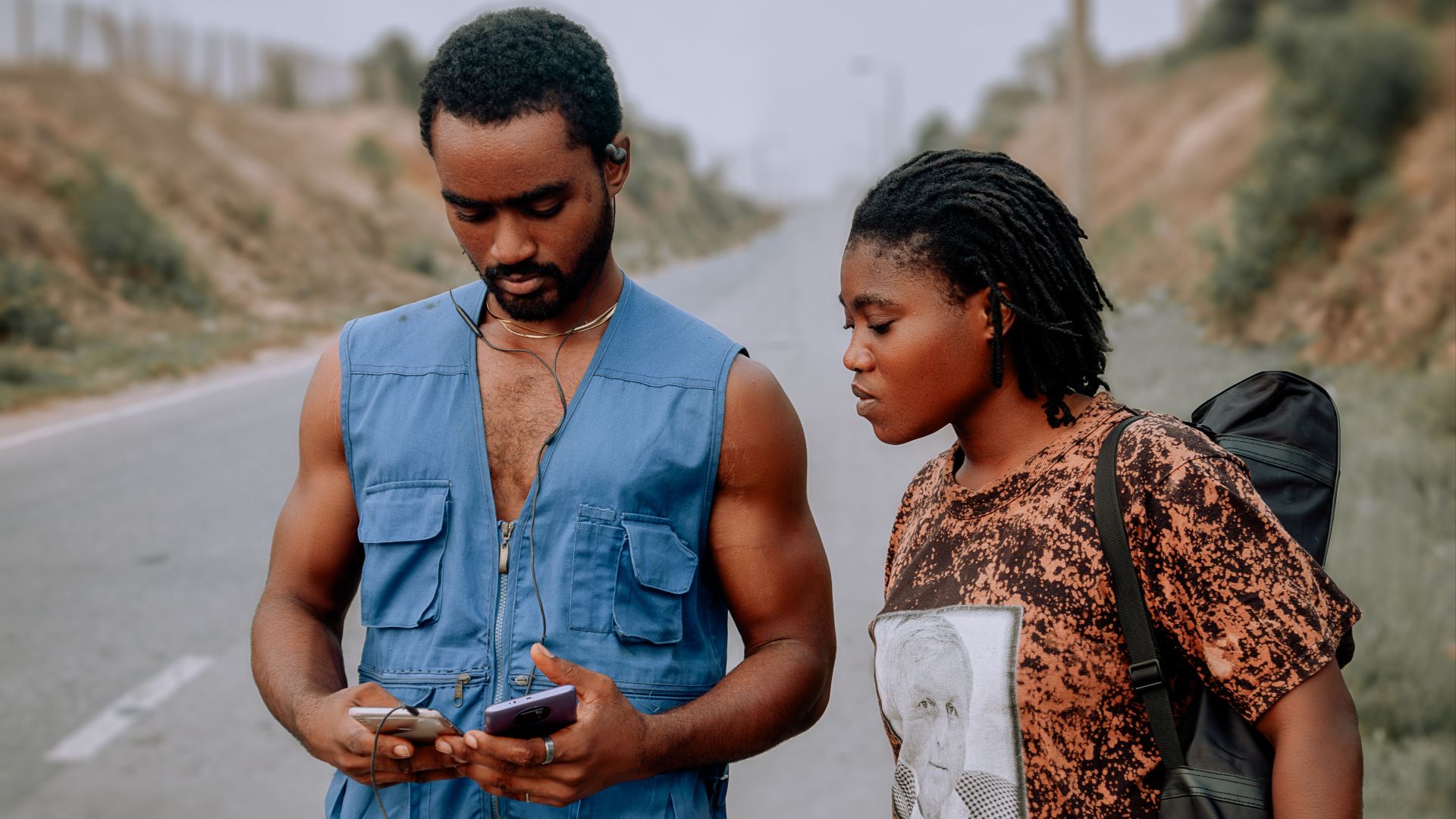 A young couple uses a phone for navigation on a rural road trip.