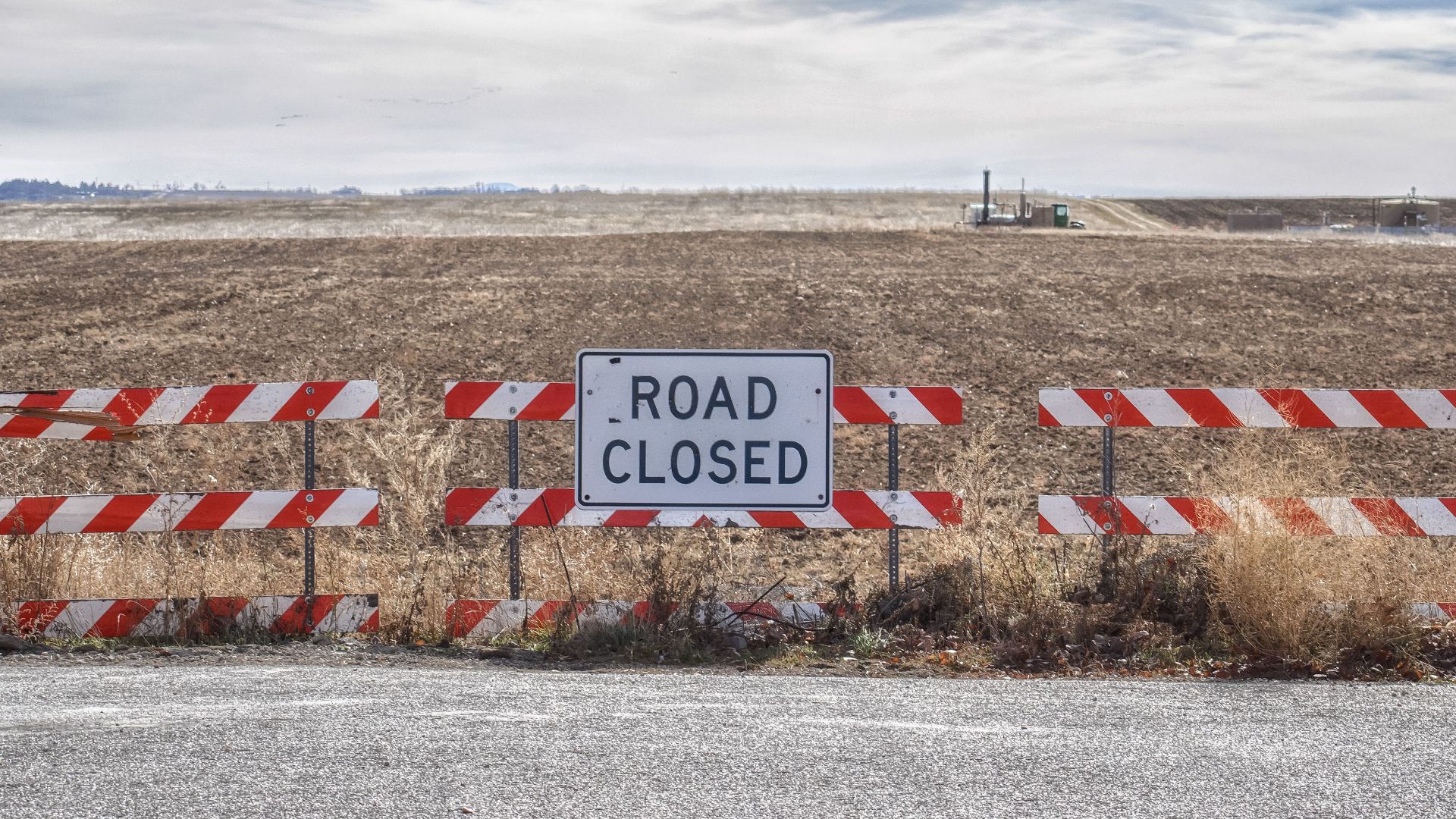 Road closed sign blocking access to a rural field under a cloudy sky.