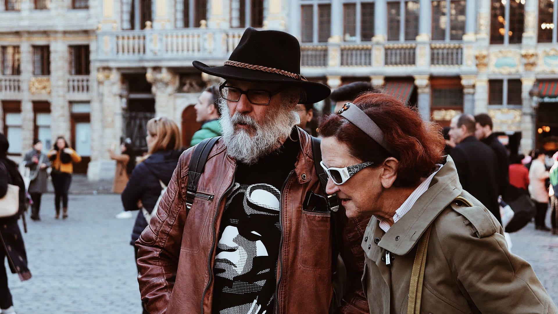 A couple in stylish attire exploring a bustling European city square, capturing urban travel moments.