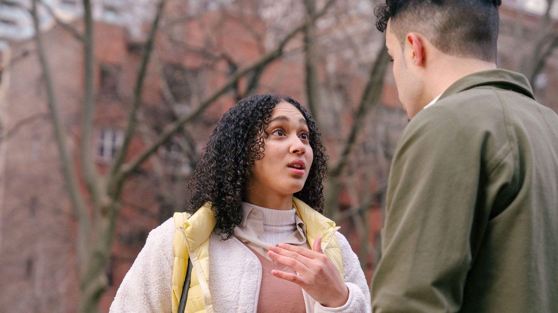 From below of ethnic female with short curly hair standing and arguing with boyfriend on street in daylight