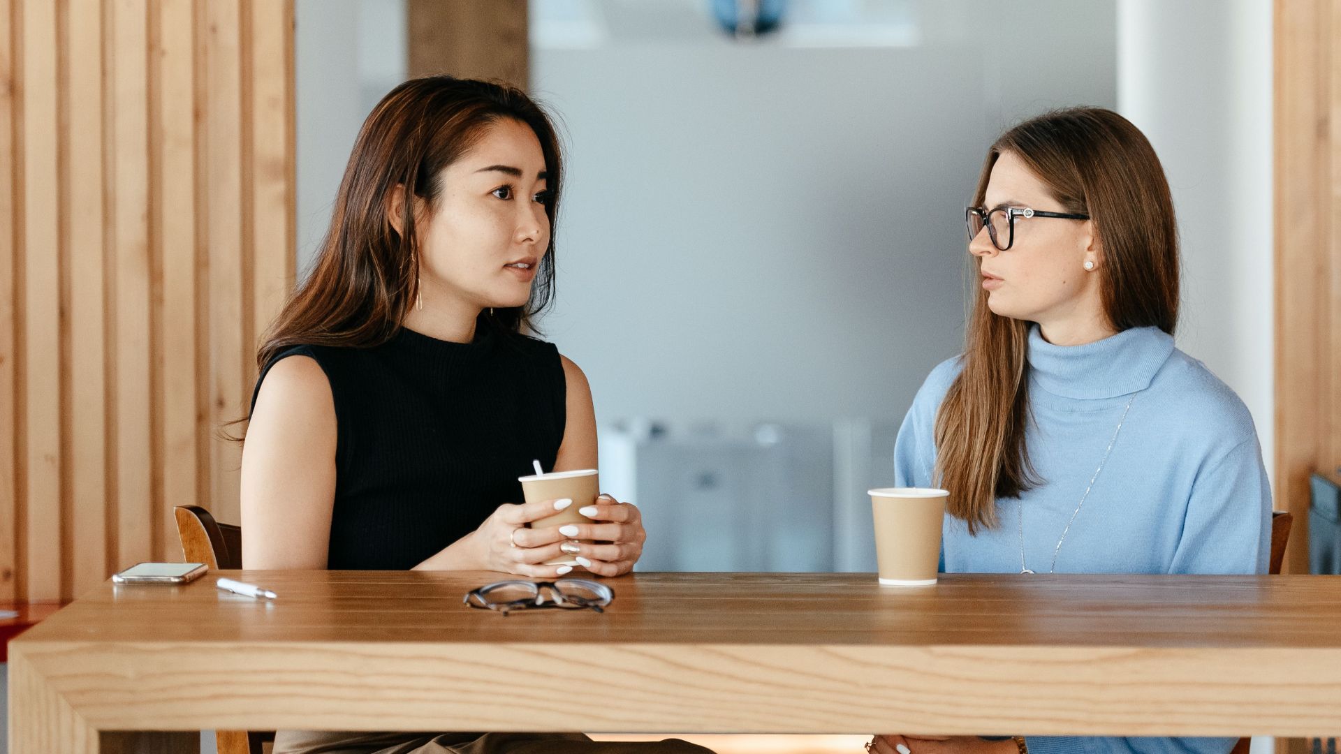 Young multiracial friends speaking at wooden table with cups of hot coffee in cafe