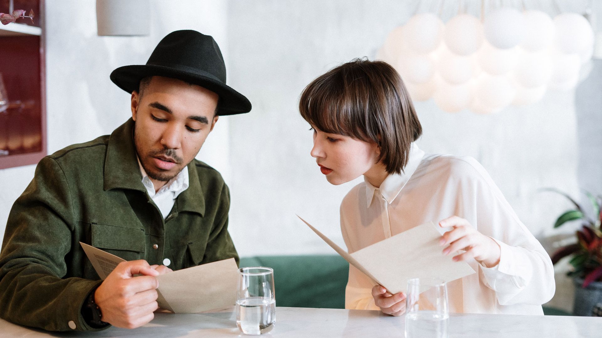 A couple reviews the menu in a modern cafe setting, discussing their meal choices.