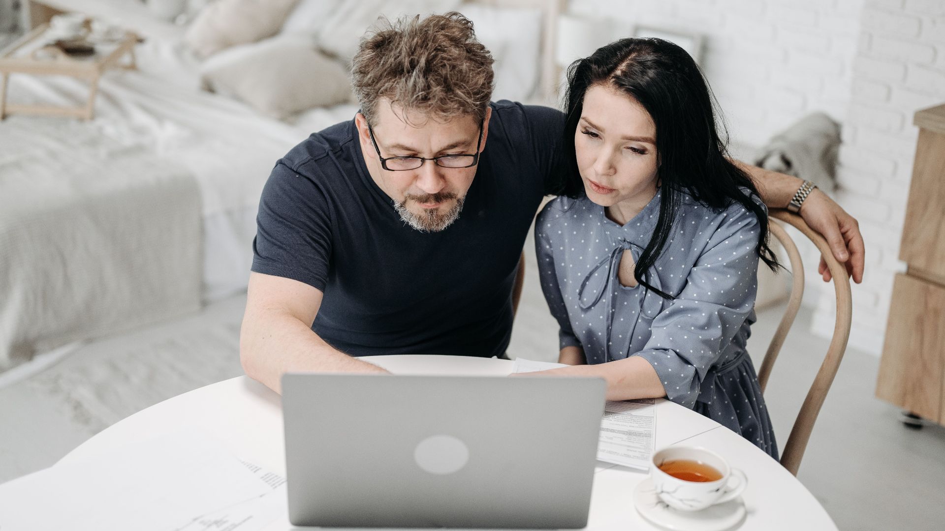 Couple working together on a laptop at home, discussing plans over tea.