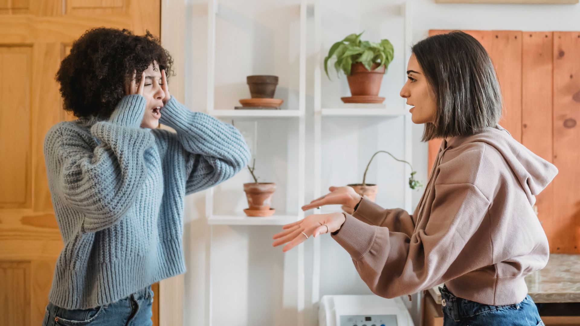 Side view of African American woman with closed eyes quarreling with female wile standing in light room near kitchen at home