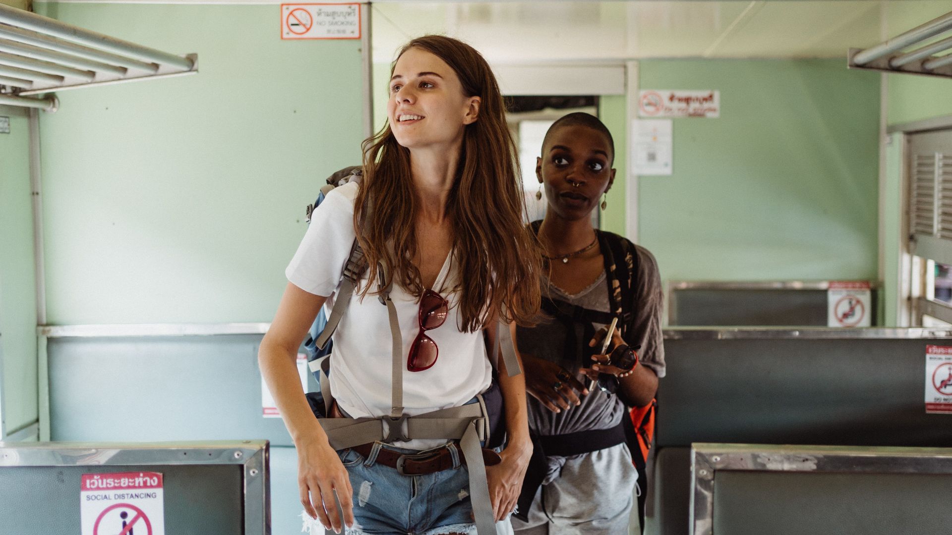 Two young women enjoy a train journey in Thailand, exploring local travel experiences.