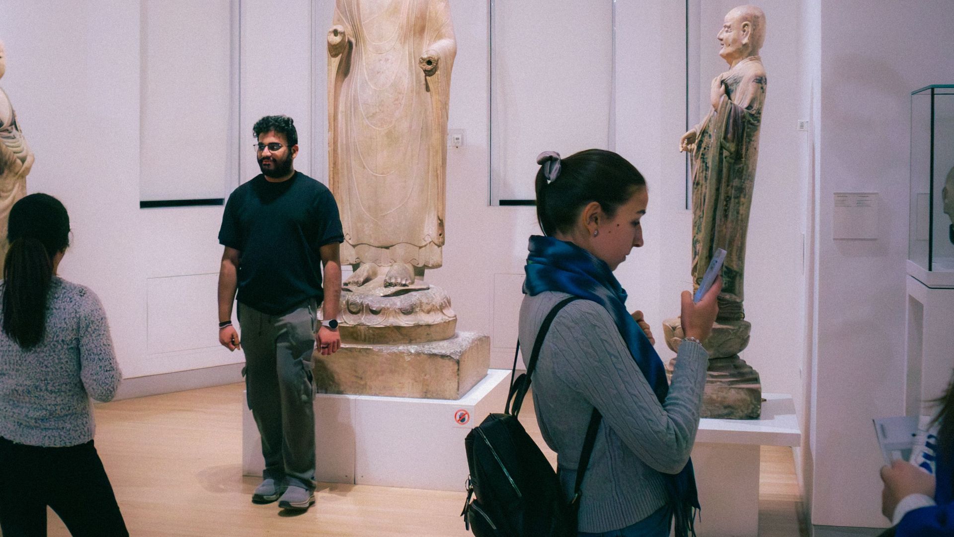 People exploring a Toronto art museum showcasing historic Buddha statues from Chinese culture.