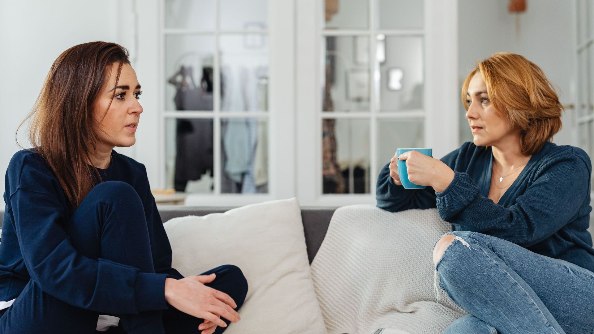 Two women enjoying a casual conversation on the couch, sipping tea and snacking indoors.