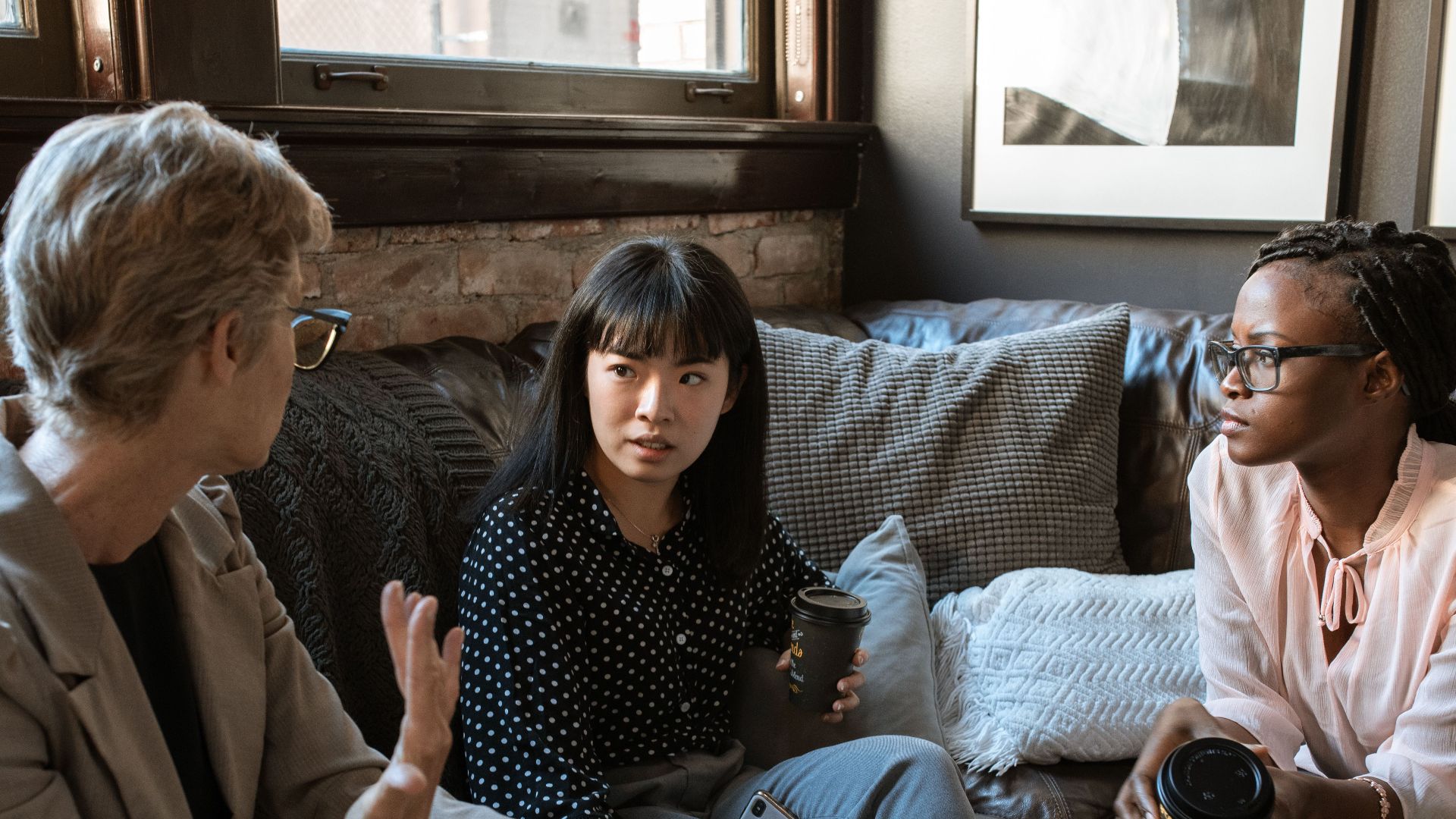 Three women of different ethnicities engaging in a discussion in a cozy living room setting.