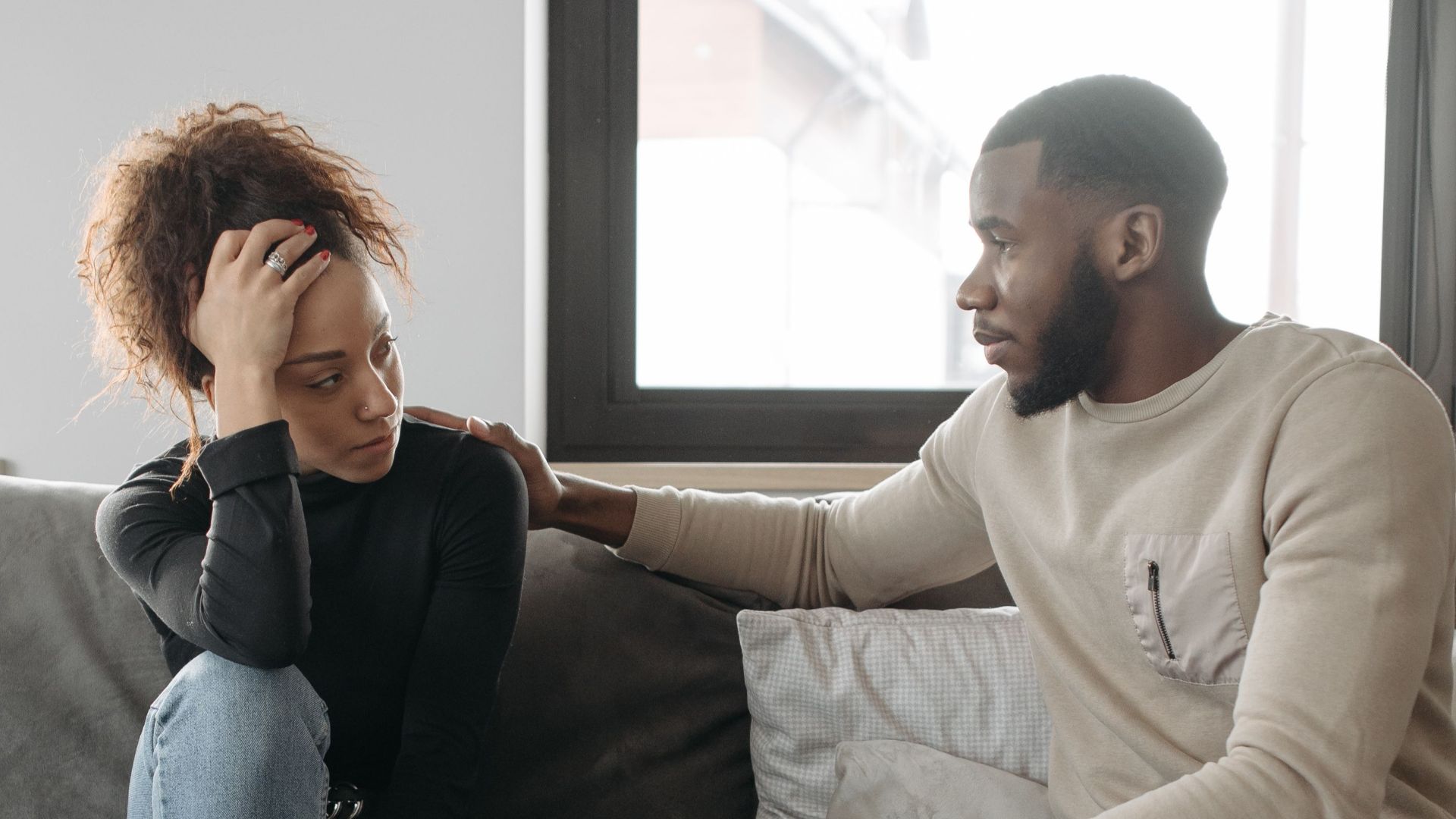 A couple shares a moment on their sofa at home, conveying care and understanding.