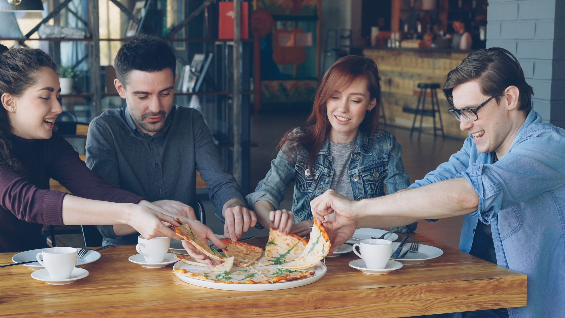 A group of friends enjoying pizza and coffee in a casual café setting.