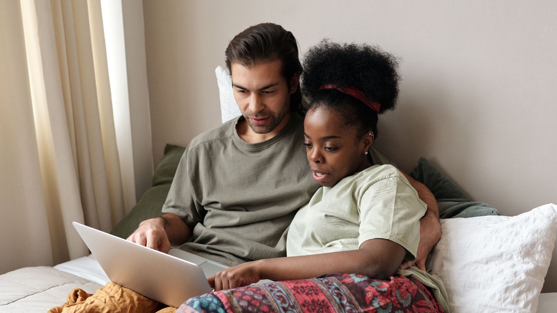 A couple enjoying leisure time together on a bed using a laptop, signifying modern relaxation.