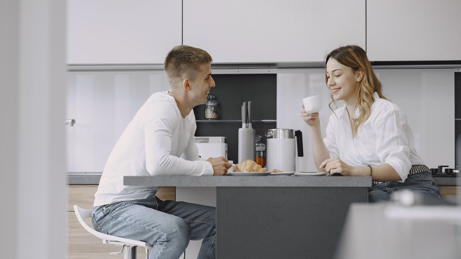 Smiling couple enjoying breakfast and coffee in their modern kitchen, promoting a sense of comfort and togetherness.