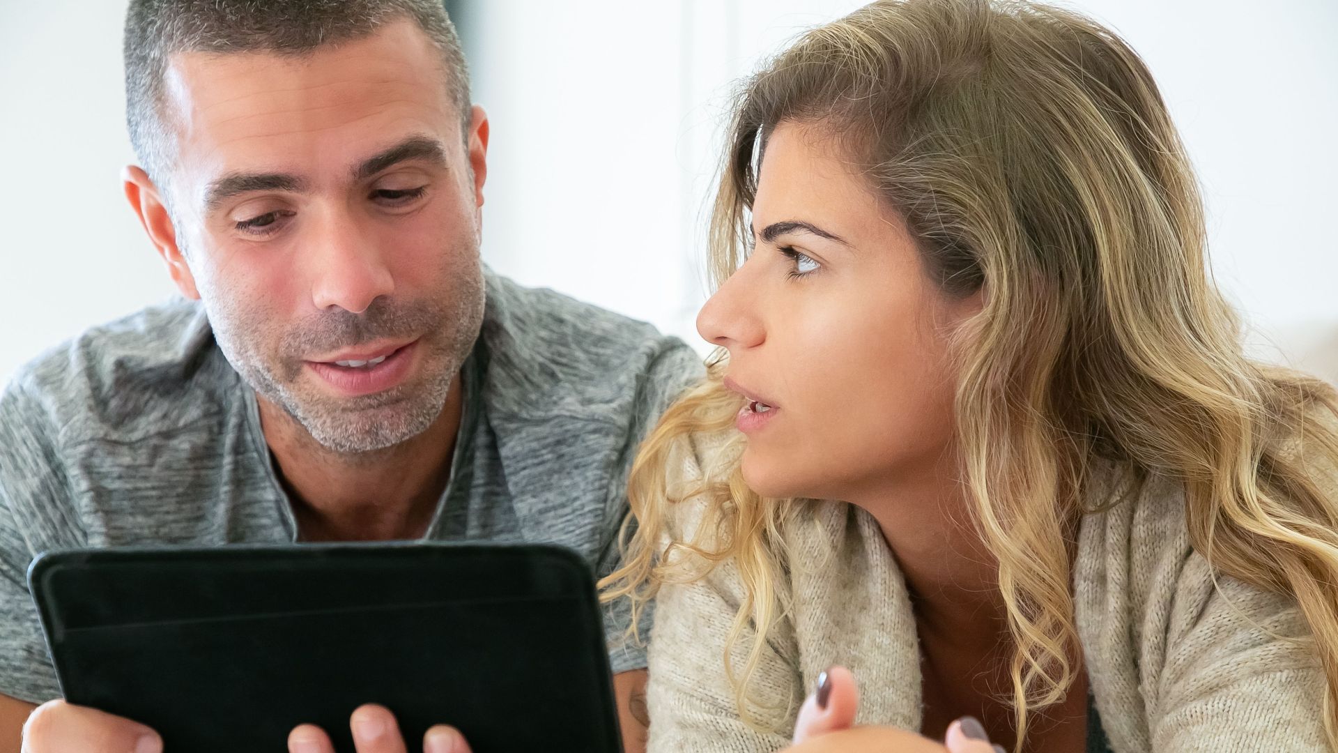 A couple engaging in conversation while using a tablet at home, focusing on digital collaboration.