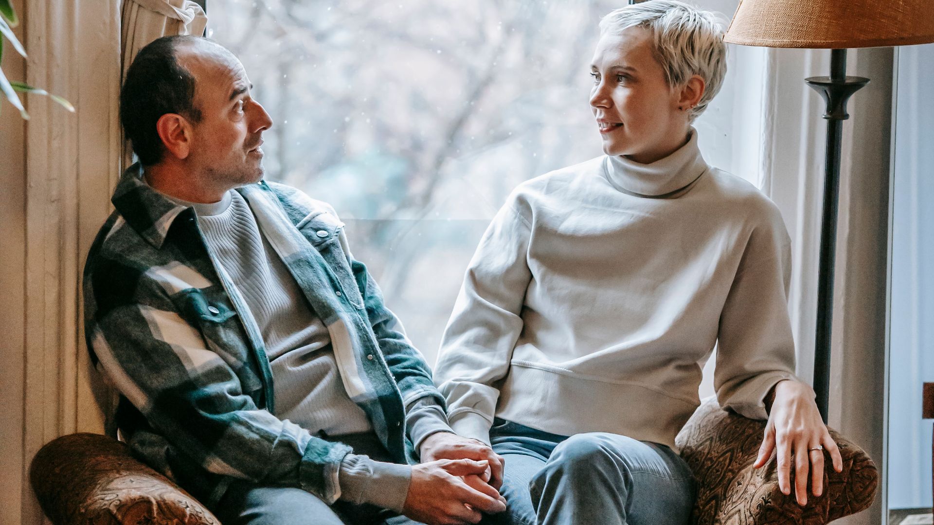 Full body of cheerful middle aged couple relaxing on couch while speaking in cozy lounge